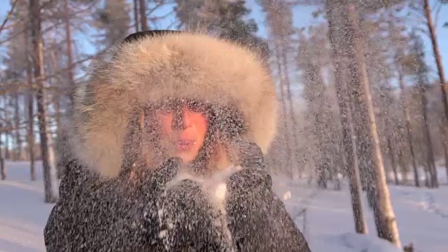 慢镜头:冬日里，一名年轻女子向镜头里吹着闪闪发光的雪花视频下载
