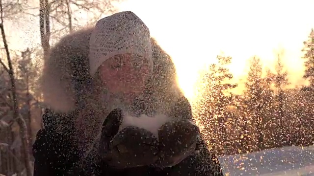 慢镜头:一名年轻女子在神奇的冬日日出中吹着闪闪发光的雪花视频素材