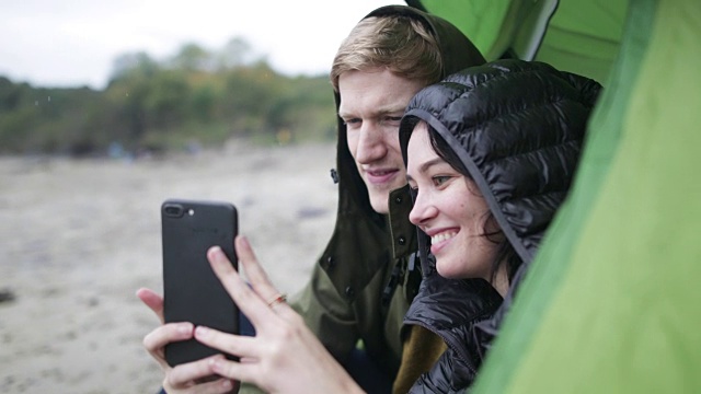 一对年轻夫妇在露营旅行中使用智能手机视频下载