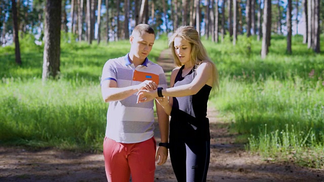 一对穿着运动服的年轻夫妇在一个阳光明媚的日子里跑过森林，一位女运动员问一位男士他们已经跑了多远视频下载