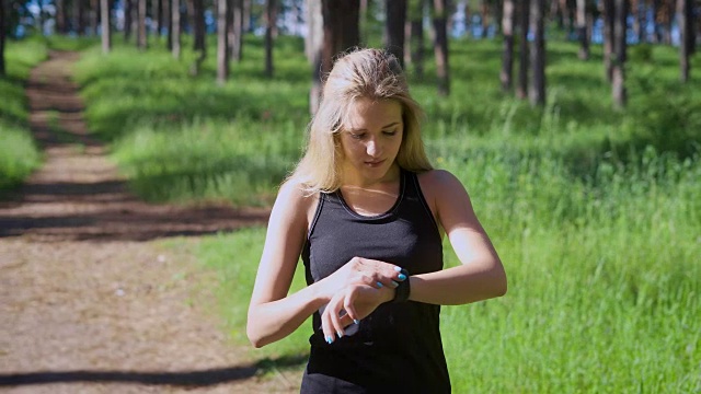 一个年轻的金发女人改变智能手表上的设置，一个跑步的运动员想知道她跑了多少公里视频下载