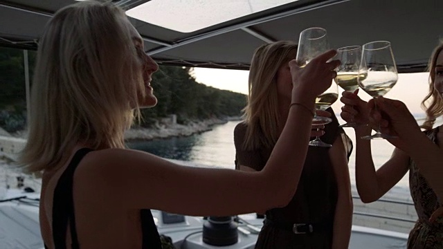 快乐的年轻女人和男人在游艇上庆祝，他们碰杯和祝酒。美丽的自然和海滨景色。视频下载