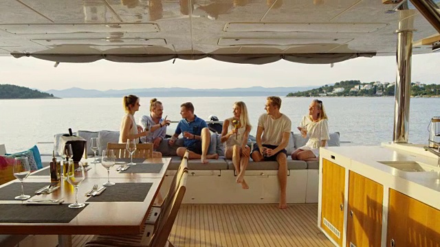 一群成功的年轻人在游艇尾部享受美好时光，他们喝鸡尾酒，聊天，玩得开心。在背景海洋和岛屿。视频素材