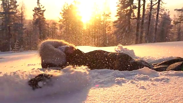 慢动作顽皮的女孩在金色的夕阳下在新鲜的雪中制造雪天使视频素材