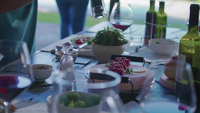人们喝酒、吃饭、聊天的细节。四个白人朋友男女地中海意大利沙拉，肉排和面包午餐或晚餐。夏日派对在现代家庭4k掌上视频视频素材