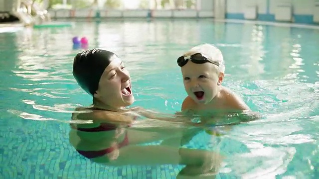 快乐的小男孩和他的妈妈在游泳池里游泳。她抱着他，教他游泳。幸福的家庭一起度过时光视频素材
