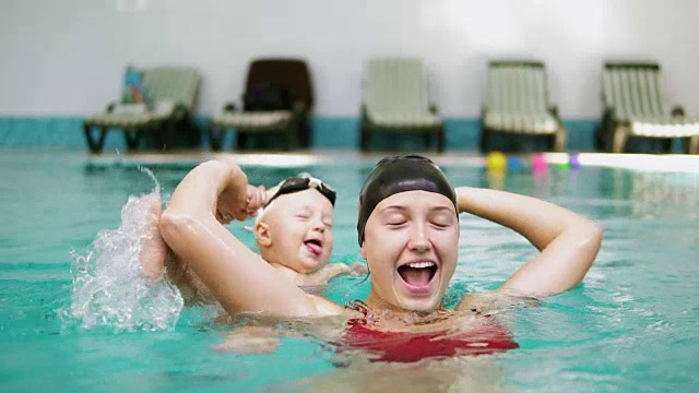 慢动作拍摄的快乐微笑的孩子和他的母亲在游泳池游泳。年轻的妈妈正在水里给他转个身，和他一起玩视频素材