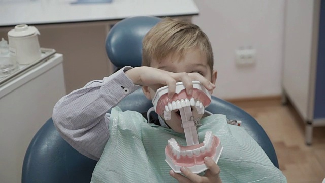 快乐的小男孩在牙医椅上玩塑料人下巴视频下载