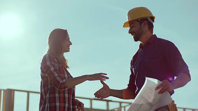 一名男子和一名女子在背景中与建筑工地握手视频素材