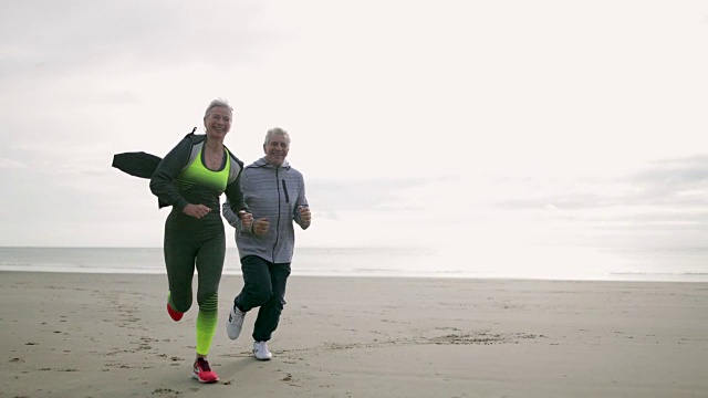 一对老年夫妇在海滩上慢跑视频素材