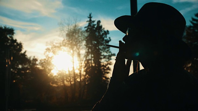 一个女孩的剪影点燃和吸烟的夕阳慢镜头视频素材