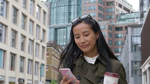亚洲女商人走在城市里，看着智能手机。视频素材