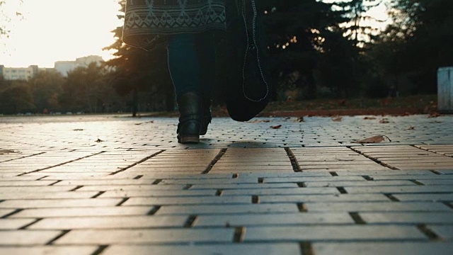 低角度观看慢动作拍摄的女性腿在牛仔裤和靴子走离相机在日落视频下载