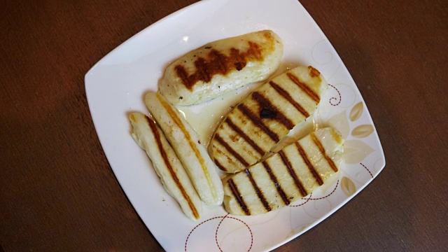 烤哈洛米奶酪片在盘子上俯视图旋转。米色盘子上烤希腊山羊奶酪。条纹金棕色。食物mediterian厨房。视频下载