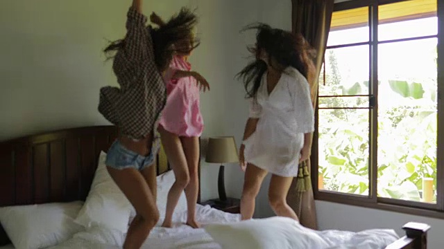 女孩们在卧室的床上跳舞和蹦蹦跳跳，年轻快乐的女性朋友们开心地笑着视频下载
