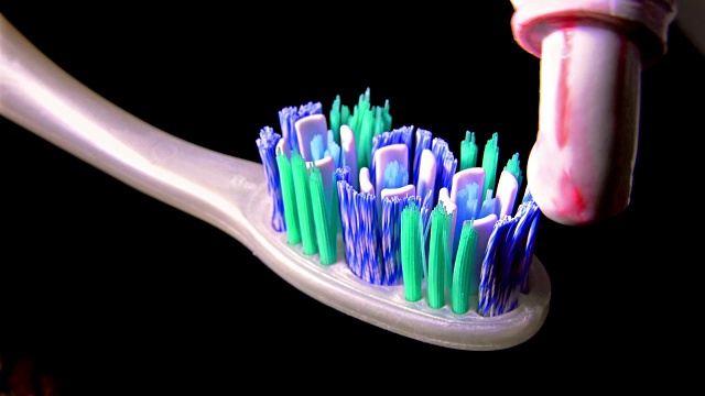 在黑色背景上牙膏被挤到牙刷上的细节。索尼超高清拍摄，库存视频视频下载