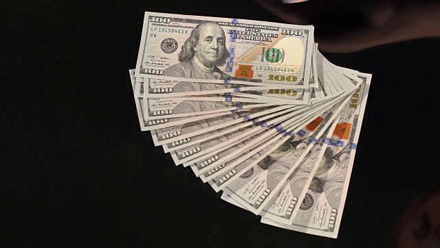 女人从一张黑色的桌子上捡起一堆美元。视频素材