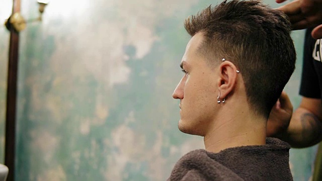 侧面的年轻英俊的白人男子在他的耳洞得到他的头发打扮和造型的胡子理发师在一个复古时尚的理发店视频下载