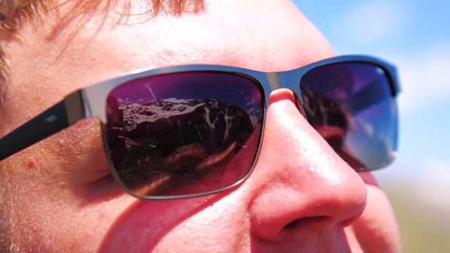 男人戴着墨镜。太阳眼镜里的山的倒影视频下载