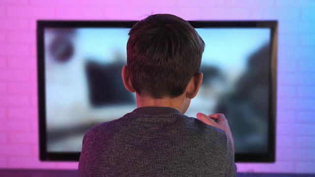 一个小男孩在电脑前玩射击视频游戏的后视图视频下载