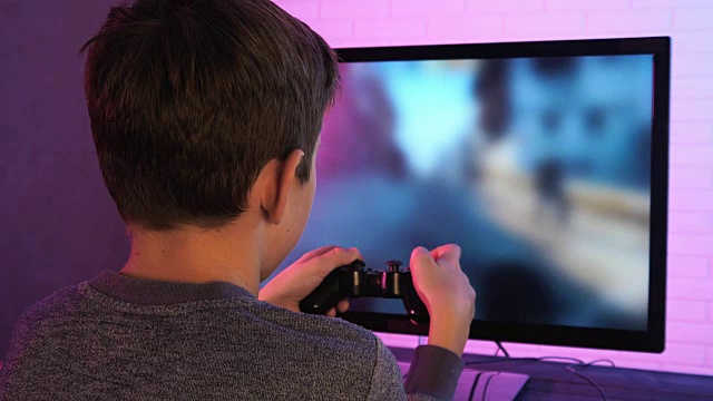一个小男孩在电脑前玩射击视频游戏的后视图视频下载