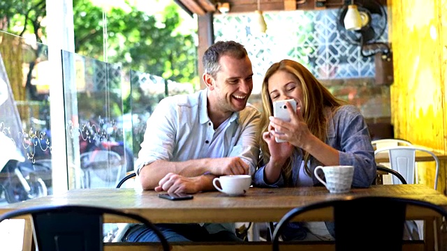 一对幸福的情侣在自助餐厅喝咖啡，在智能手机上看照片视频素材