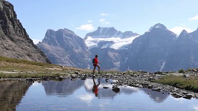 一个女人沿着一个高山湖泊徒步旅行，远处有雪山。视频素材