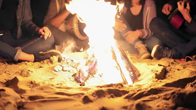深夜篝火的特写镜头。年轻人晚上坐在火炉边，弹吉他。快乐的朋友唱歌，聊天，一起玩乐视频素材