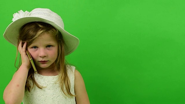 可爱的小女孩用手机上的色度键背景。小女孩穿着一件浪漫的连衣裙。白色的帽子和婚纱。色度键背景。视频下载