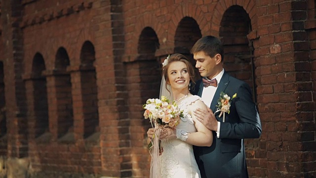 可爱的新婚夫妇站在一起，靠近古老的红色石墙视频下载