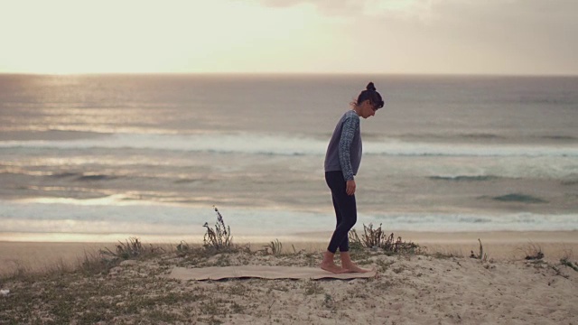美丽的中年妇女展开瑜伽马特，在日落在大西洋在法国南部的沙丘上练习瑜伽。视频下载