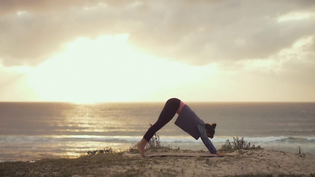 美丽的中年妇女在日落时在法国南部大西洋的沙丘上练习瑜伽。视频下载
