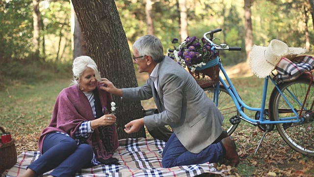 一对浪漫的老夫妇坐在草地上，一边野餐一边放松。视频素材