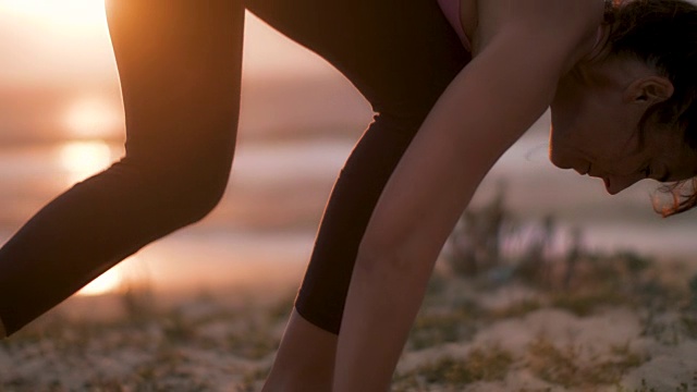美丽的中年妇女在海滩上练习瑜伽日落在大西洋在法国南部。视频下载