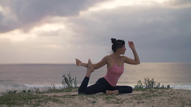 美丽的中年妇女在海滩上练习瑜伽日落在大西洋在法国南部。视频下载