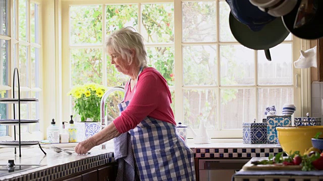 一位高级妇女在厨房里用毛巾擦干餐具视频素材
