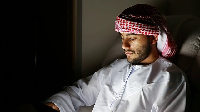 年轻的阿拉伯人在黑暗的房间里使用数码平板电脑视频下载