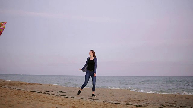 迷人的年轻女子长头发拿着五颜六色的风筝在天空中飞行，在傍晚日落时在海滩上散步。Slowmotion拍摄视频素材