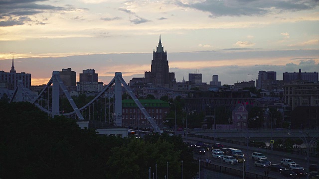 美丽的日落到夜晚过渡到莫斯科市中心的天际线。高尔基公园附近克里米亚大桥上的交通堵塞。外交部著名的七姐妹剪影视频下载