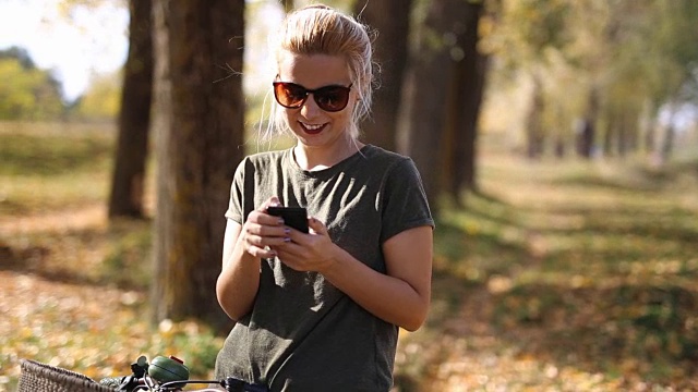 年轻的金发女郎在秋季公园使用智能手机视频素材