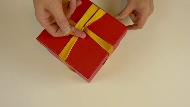 快速运动时间推移。包装红色礼品盒。白种人手工包装礼盒。男人的手在一个红色的硬纸盒上系上一条丝带。俯视图特写。金色的丝带，黄色的带子。视频素材