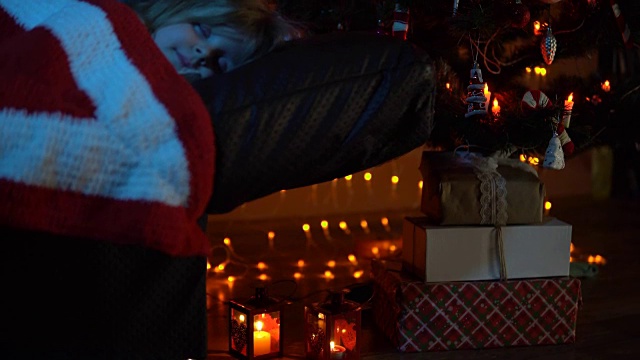 一个小女孩晚上睡在圣诞树下的地毯下的沙发上视频下载