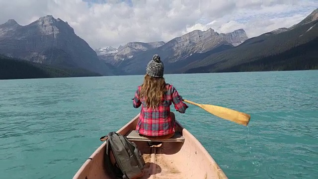 一个年轻女子划着独木舟穿过高山湖泊。视频下载