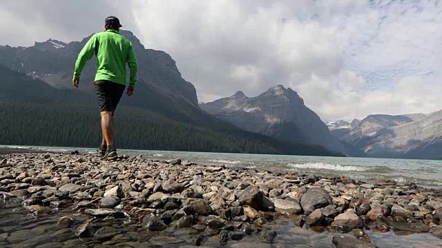 一个年轻人沿着赫克托湖的岩石海岸和远处崎岖的山脉徒步旅行。视频素材