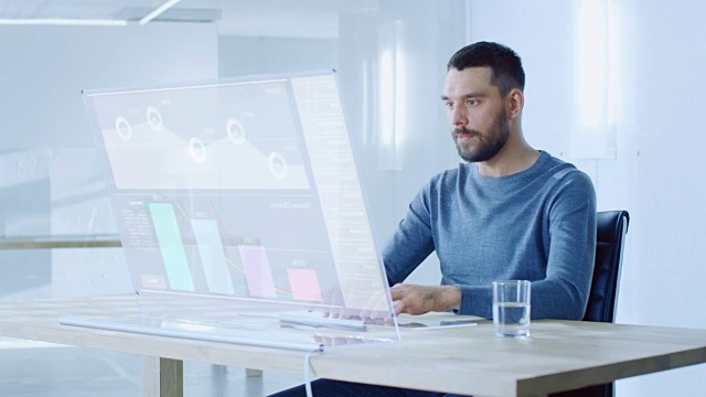在不久的将来，一个人坐在他的工作站，在他的透明显示器的现代计算机上工作。显示使用交互式图表和图形显示用户界面。视频素材