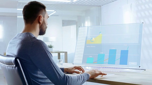 在不久的将来办公室工作人员设计透明电脑显示器的报告中。屏幕显示交互式用户界面与统计，图表和图表。办公室是明亮和现代的。视频素材