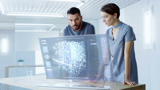 在不久的将来，男性和女性计算机工程师在透明显示计算机上工作时谈话。屏幕显示交互式神经网络，人工智能项目，未来用户界面。视频素材
