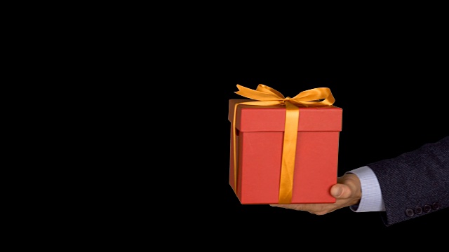 一个穿着西装的男人手里拿着一个红色礼品盒，上面有一个金色的蝴蝶结。手与礼物出现在相框中。红色的礼盒。商人送礼物。Alpha通道色度键透明背景。视频素材