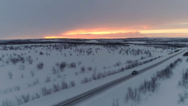 照片:日落时分，汽车在雪地上行驶，穿过风景优美的冬季穷乡僻岭视频素材