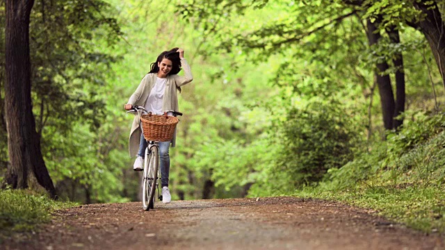 年轻无忧无虑的女人骑着自行车穿过公园。视频下载